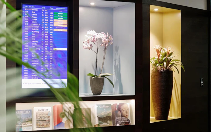 Flight information display and decorative plants at Aspire ONE Lounge, Zurich Airport.