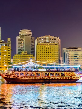Traditional dhow boat illuminated on Dubai Creek with city skyline in the background.