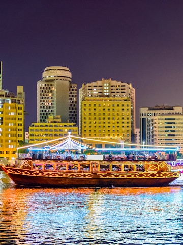 Traditional dhow boat illuminated on Dubai Creek with city skyline in the background.