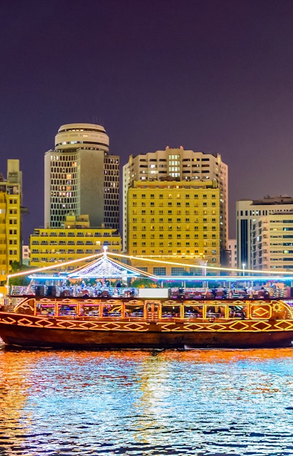 Traditional dhow boat illuminated on Dubai Creek with city skyline in the background.