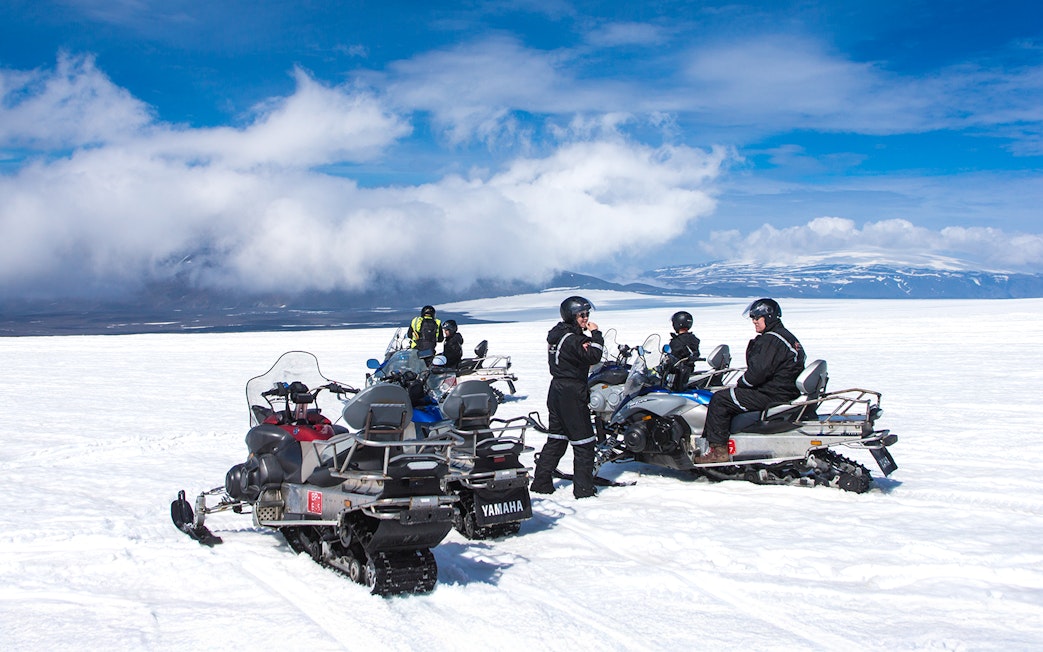 Snowmobile riders on Langjokull Glacier, Iceland, with snowy landscape and blue sky.