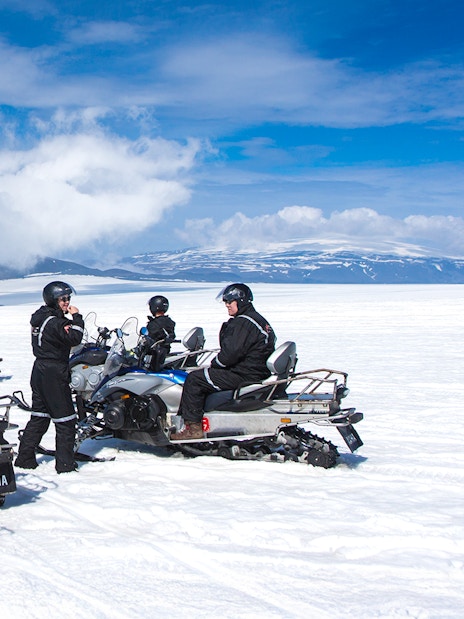 Snowmobile riders on Langjokull Glacier, Iceland, with snowy landscape and blue sky.