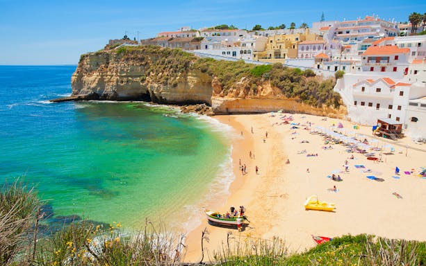 Sandy beach with colorful boats and cliffs on the Algarve Coast, Portugal.