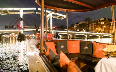 Evening canal cruise boat with illuminated bridge in Amsterdam during winter.