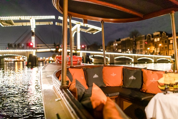 Evening canal cruise boat with illuminated bridge in Amsterdam during winter.