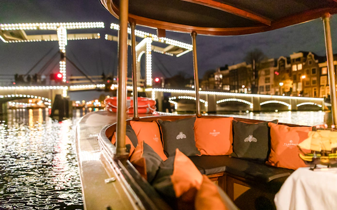 Evening canal cruise boat with illuminated bridge in Amsterdam during winter.