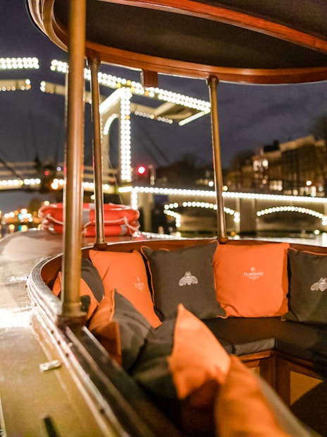Evening canal cruise boat with illuminated bridge in Amsterdam during winter.
