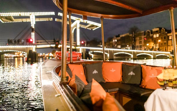 Evening canal cruise boat with illuminated bridge in Amsterdam during winter.