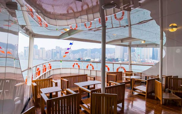 Star Ferry deck with wooden seating, overlooking Hong Kong skyline across Victoria Harbor.
