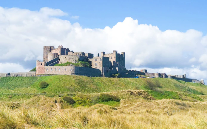 Bamburgh Castle exterior on a grassy hill under a blue sky.