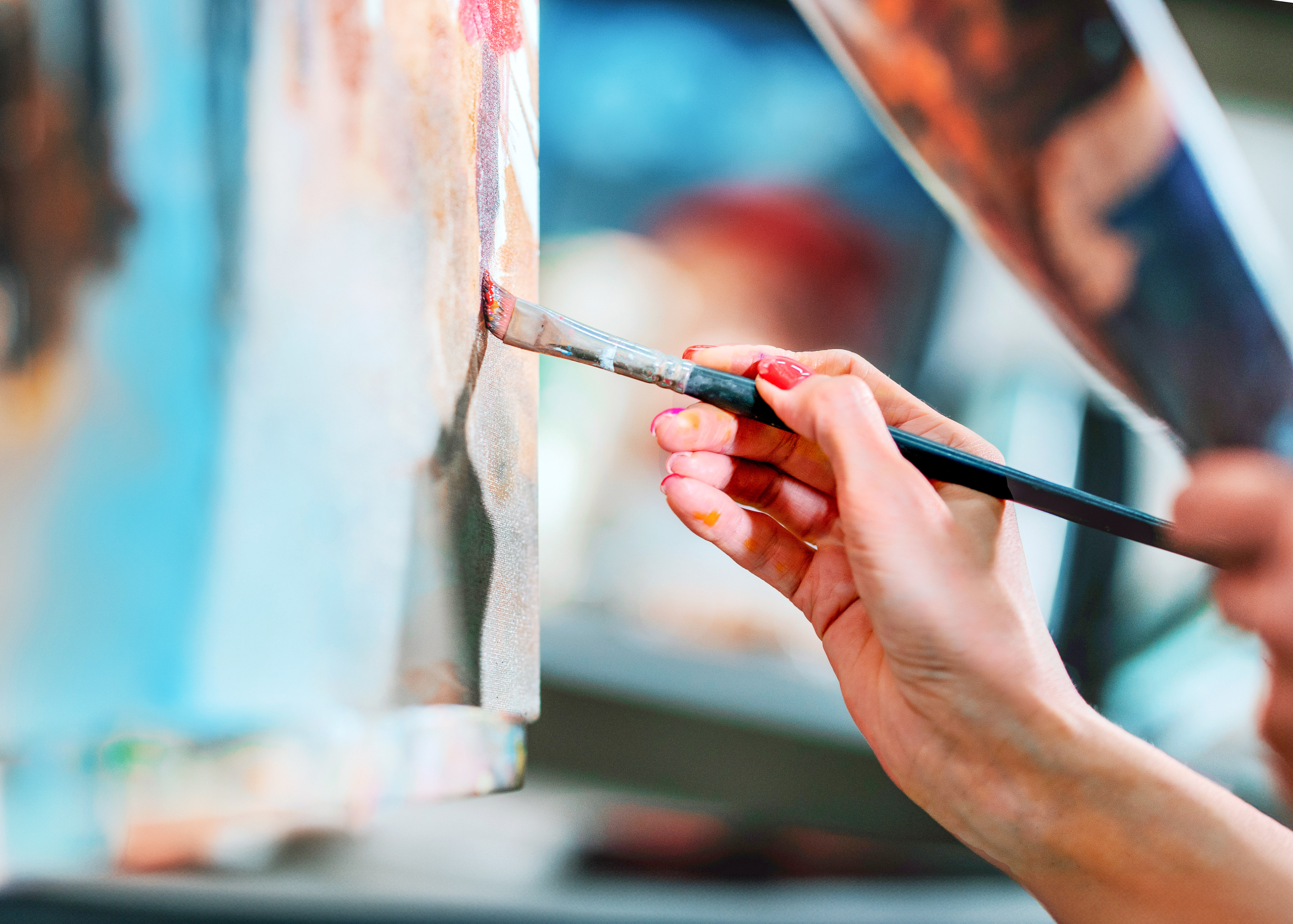 Young artist's hand painting on canvas with a brush.