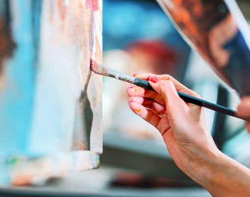 Young artist's hand painting on canvas with a brush.