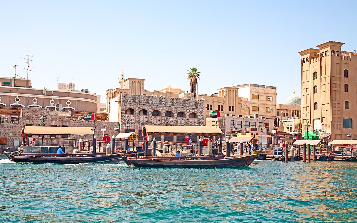 Traditional abras on Dubai Creek with historic buildings in the background, showcasing Dubai culture and tradition.