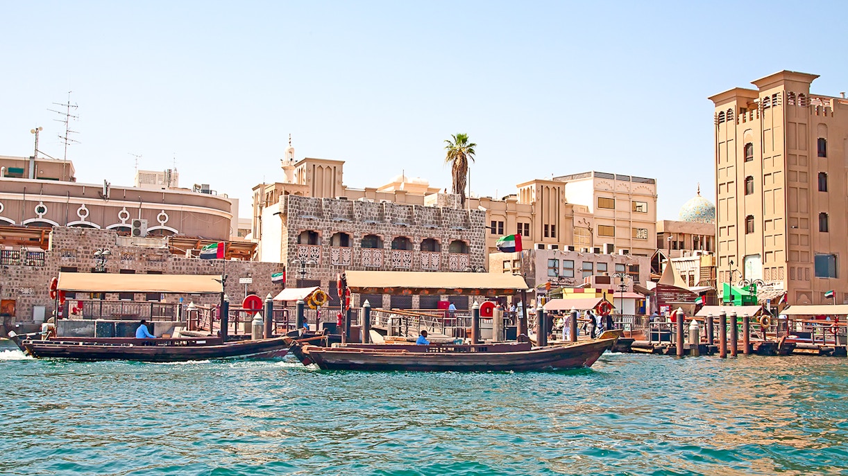 Traditional abras on Dubai Creek with historic buildings in the background, showcasing Dubai culture and tradition.