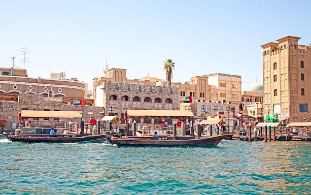 Traditional abras on Dubai Creek with historic buildings in the background, showcasing Dubai culture and tradition.