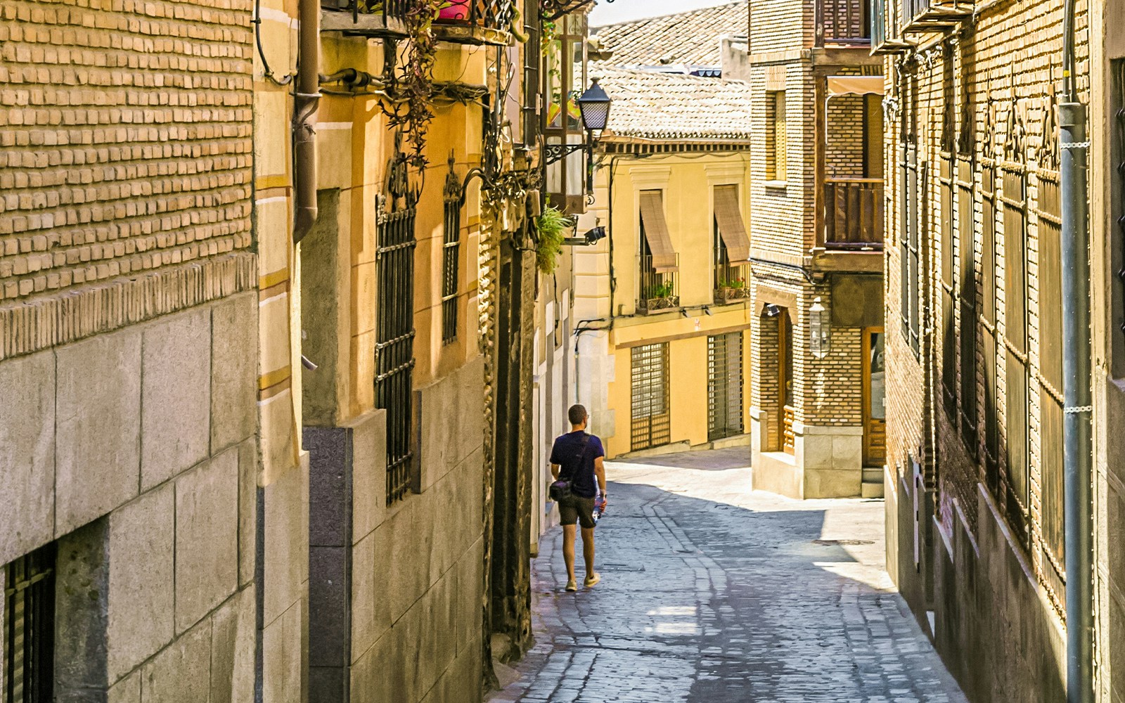 Toledo old town street with tourists strolling past historic buildings.