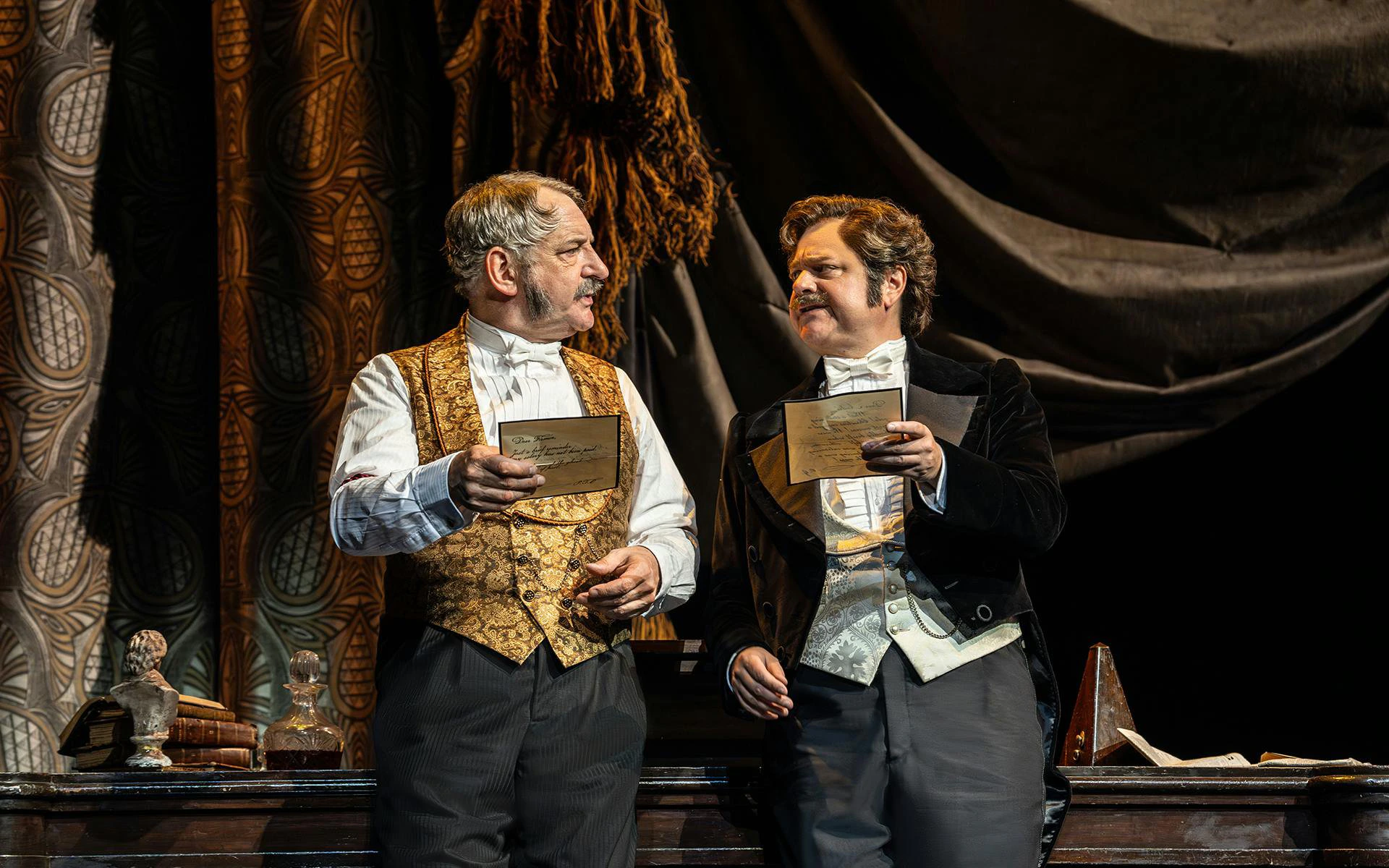 Two actors in period costumes holding letters on stage during a Phantom production.
