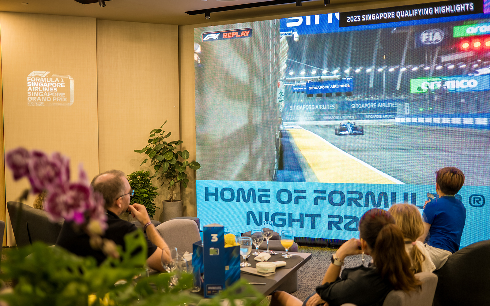Guests watching Formula 1 Singapore Grand Prix highlights on a large screen in a hospitality suite.