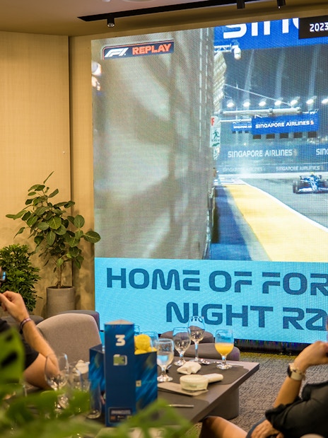 Guests watching Formula 1 Singapore Grand Prix highlights on a large screen in a hospitality suite.