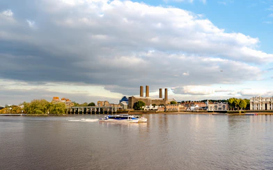 Thames River ferry passing Greenwich riverfront buildings in London.