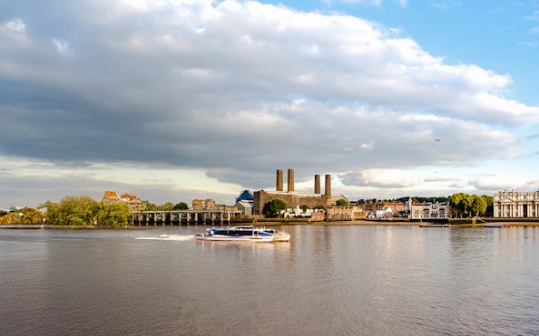 Thames River ferry passing Greenwich riverfront buildings in London.