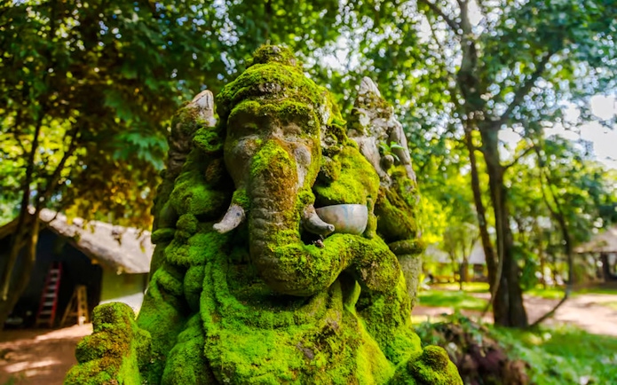 Moss-covered stone statue of Hindu deity Ganesha in a lush forest setting.