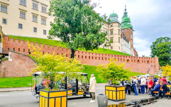Golf cart tour near Wawel Castle in Krakow with tourists gathered nearby.