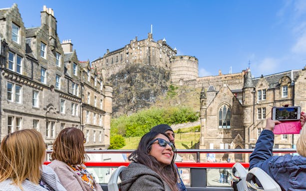 Edinburgh cityscape with iconic red hop-on hop-off bus near historic buildings.