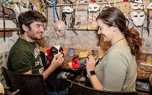 Couple painting masks at a workshop, surrounded by colorful masks and art supplies.