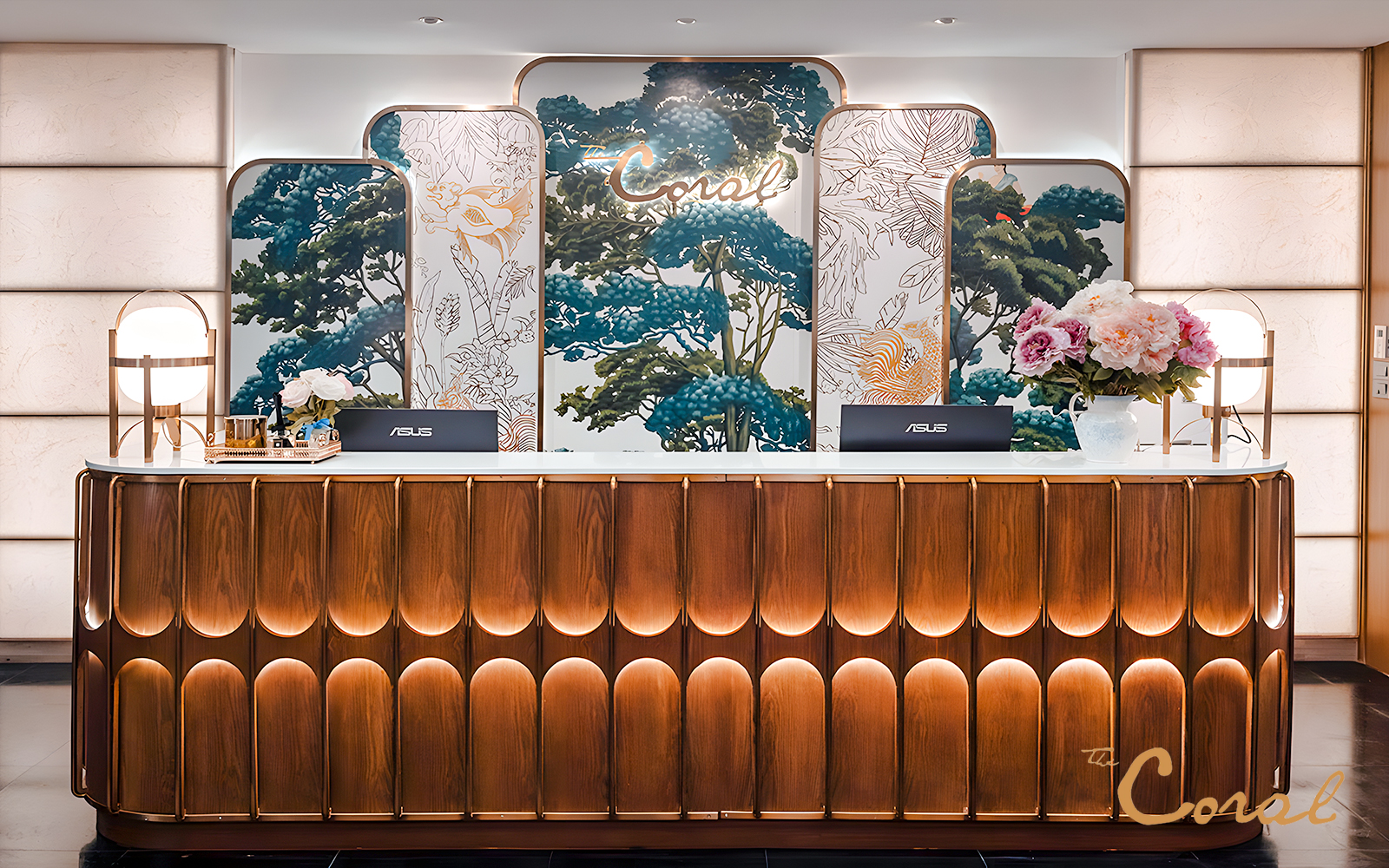 Reception desk at The Coral First Class Lounge, Bangkok airport, featuring floral decor and elegant lighting.