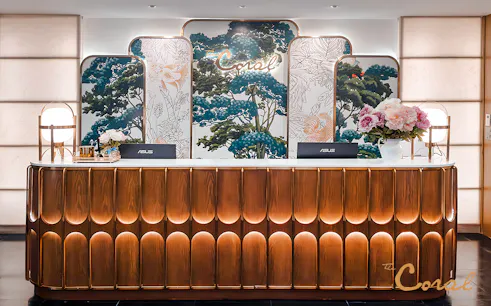 Reception desk at The Coral First Class Lounge, Bangkok airport, featuring floral decor and elegant lighting.