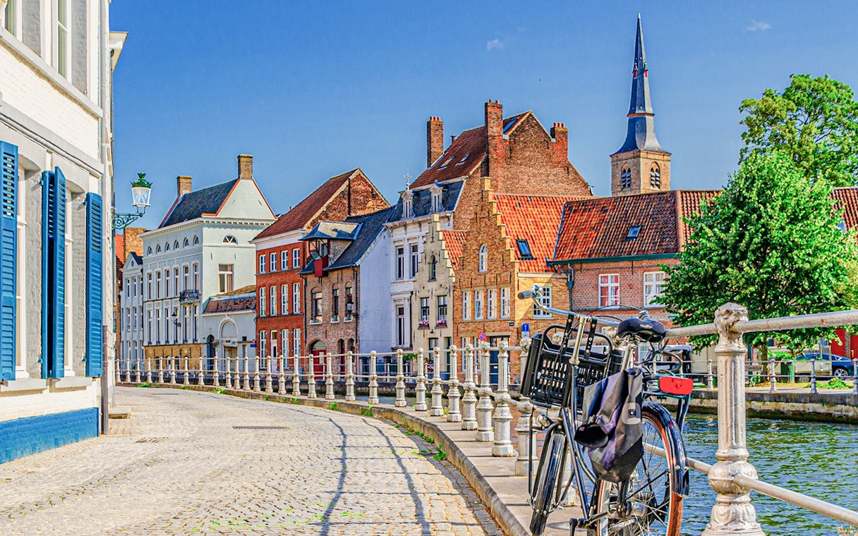 Bicycle parked along a canal in the historic center of Bruges with traditional buildings.