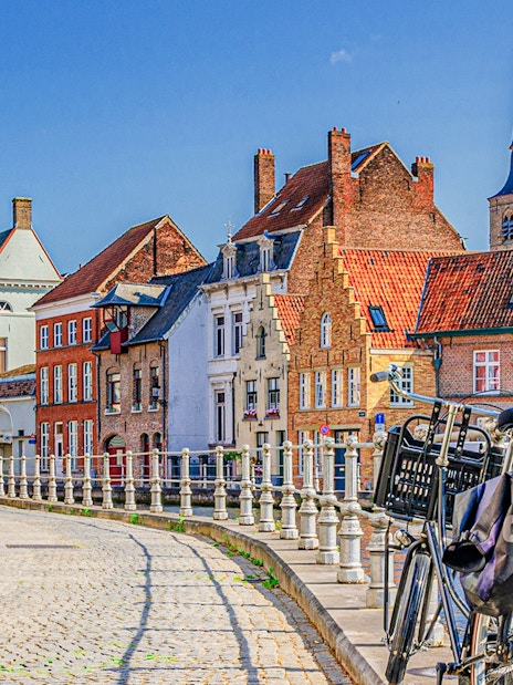Bicycle parked along a canal in the historic center of Bruges with traditional buildings.
