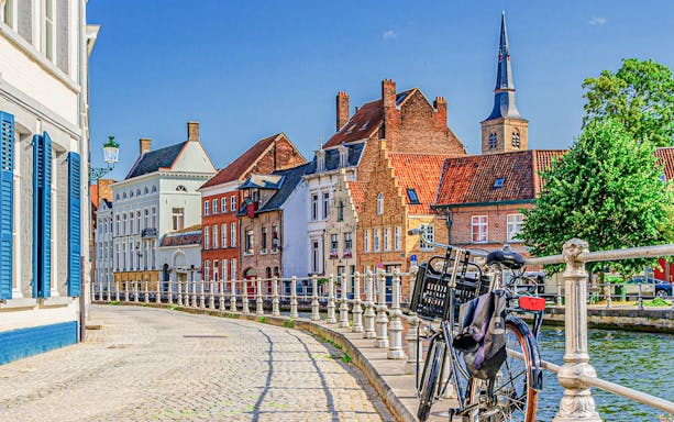Bicycle parked along a canal in the historic center of Bruges with traditional buildings.