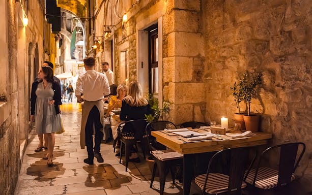 Outdoor dining in a narrow alley of Diocletian's Palace, Split, with people enjoying wine tasting.