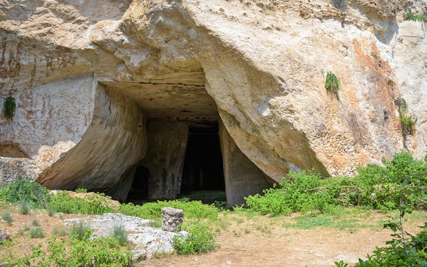 Cave entrance at Neapolis Archaeological Park, Syracuse, surrounded by greenery.