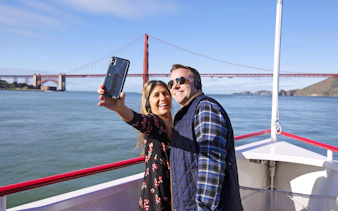Couple taking a selfie on a Golden Gate Bay Cruise with the Golden Gate Bridge in the background.