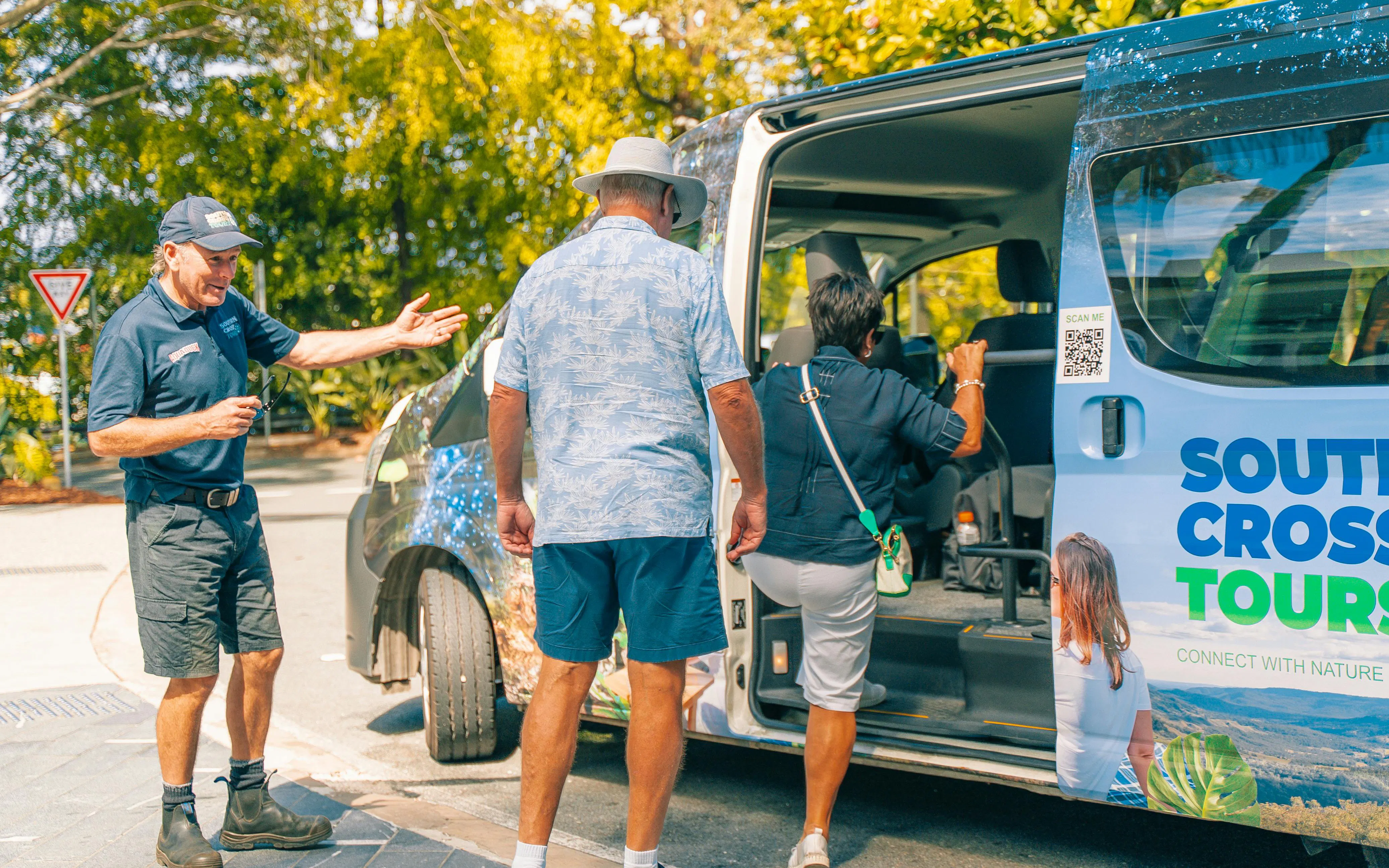 Tour guide assisting visitors boarding a South Cross Tours van at Tamborine Mountain.