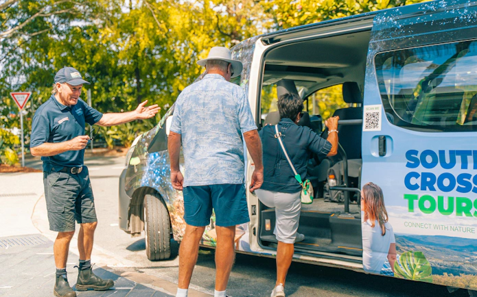 Tour guide assisting visitors boarding a South Cross Tours van at Tamborine Mountain.