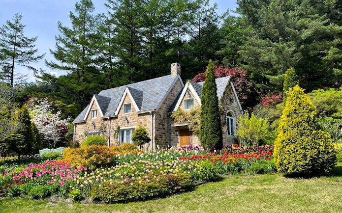 Stone cottage surrounded by colorful tulips and trees at The Garden of Morning Calm, South Korea.