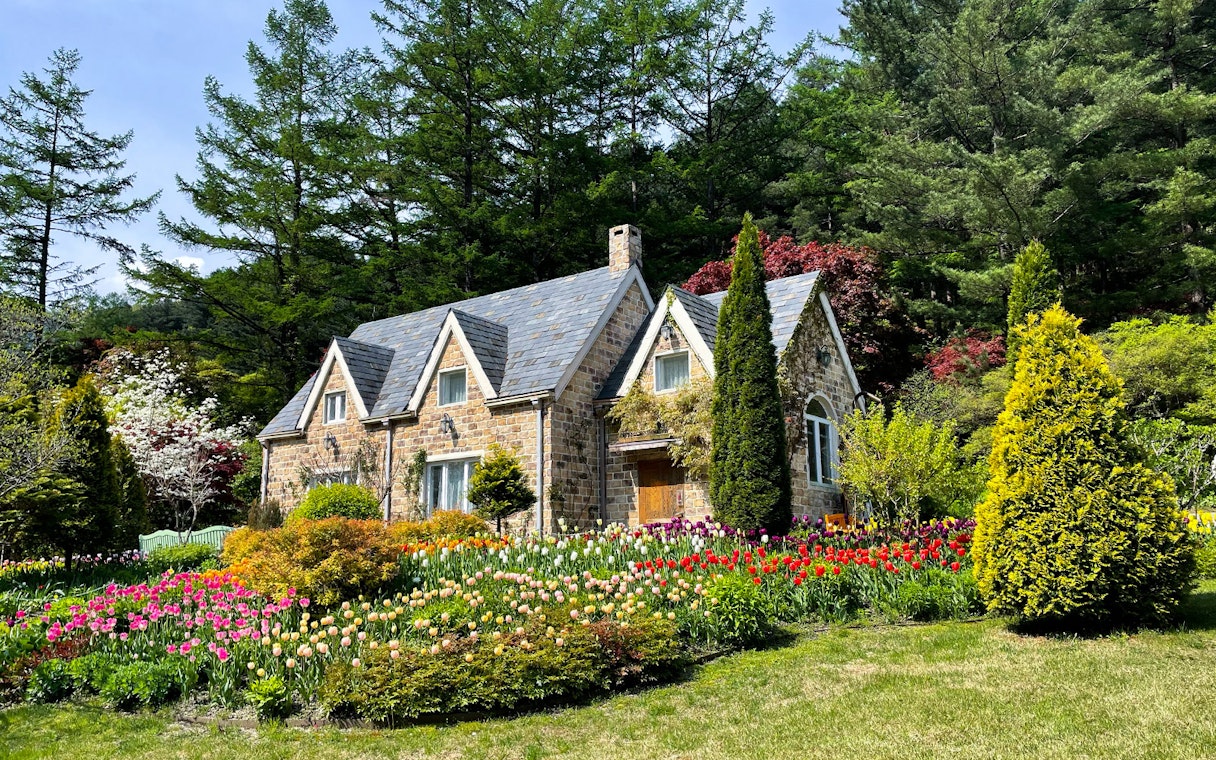 Stone cottage surrounded by colorful tulips and trees at The Garden of Morning Calm, South Korea.