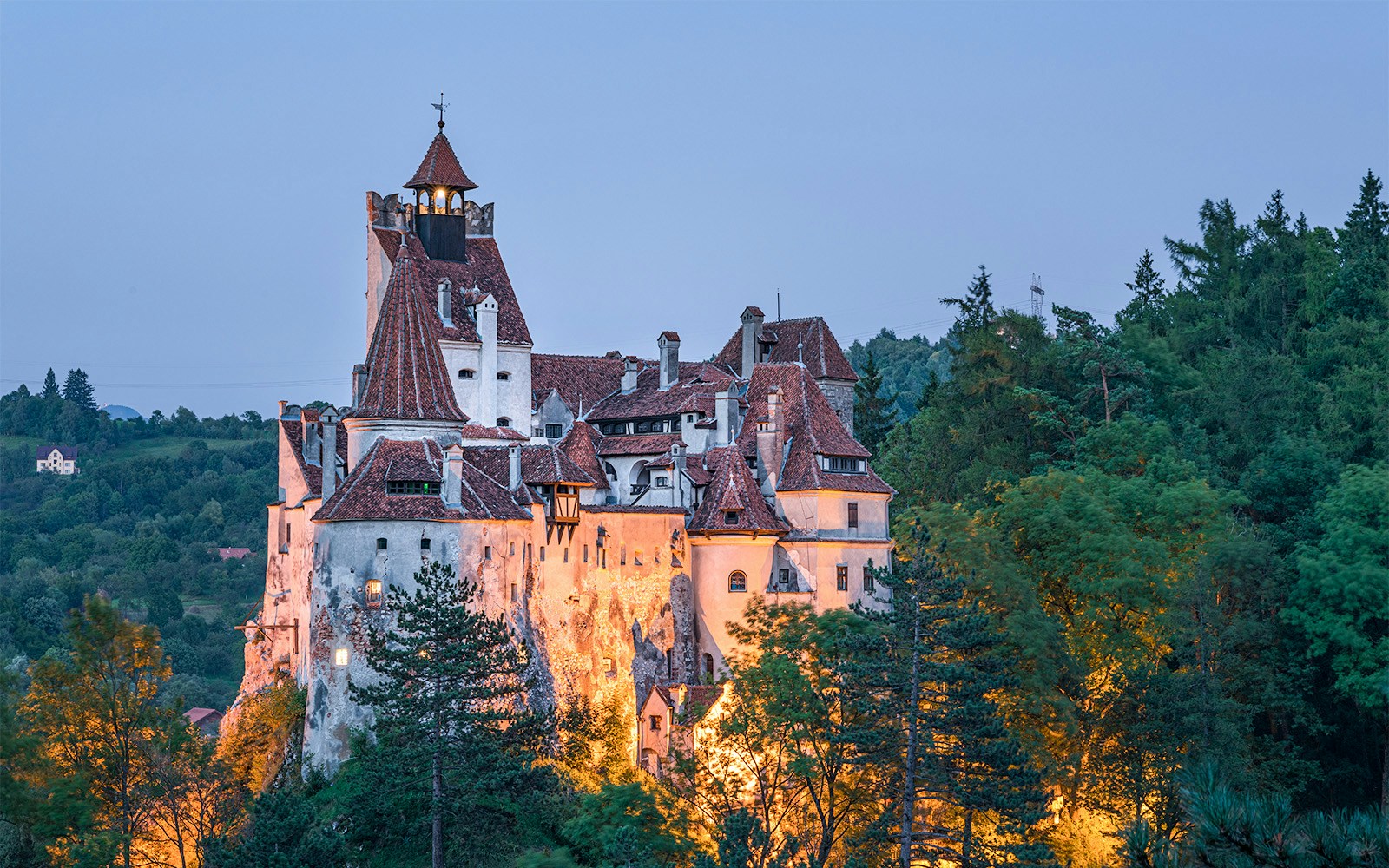 Bran Castle in Romania surrounded by lush green forest at dusk.