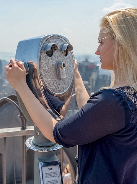 Woman viewing Manhattan skyline through binoculars at Top of the Rock, New York.