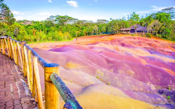 Coloured Earth hills in Chamarel, Mauritius with wooden walkway and lush greenery.