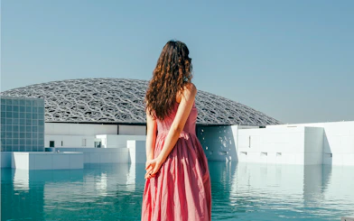 Woman standing by the water at Louvre Abu Dhabi with dome in background.