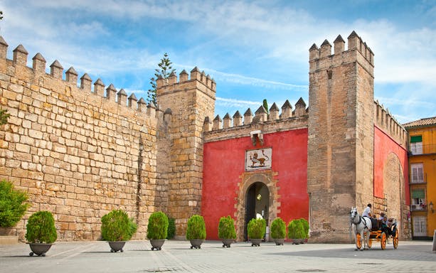 Entrance to the Royal Alcazar of Seville with stone walls and horse-drawn carriage.