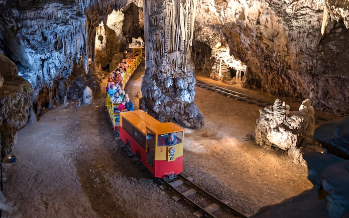 Train tour inside Postojna Cave with visitors exploring stalactites and stalagmites.