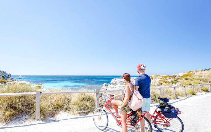 Couple cycling with ocean view on Rottnest Island, Western Australia.