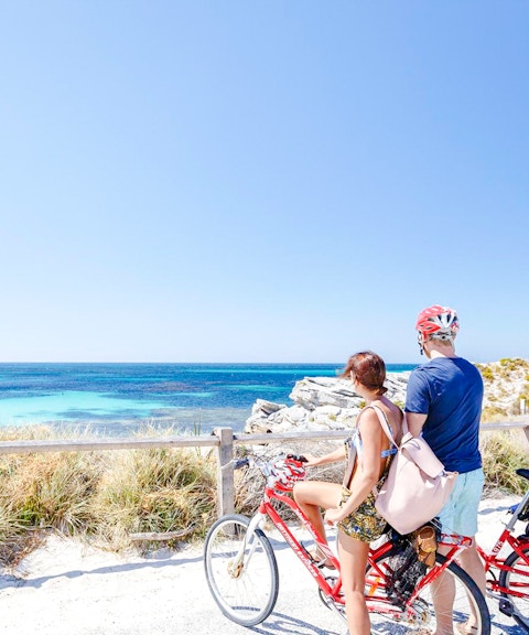 Couple cycling with ocean view on Rottnest Island, Western Australia.