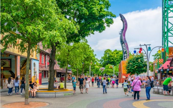 Crowded walkway at Vienna Prater amusement park with colorful attractions and trees.
